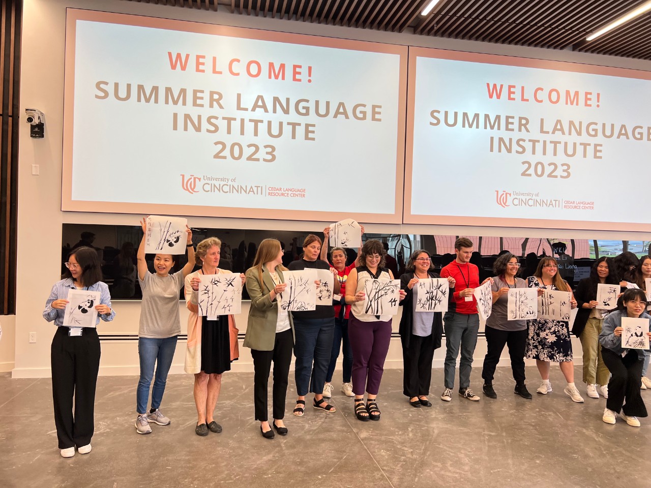 Attendees standing in front of a screen that says "Summer Language Institute 2023", holding up a paper that they drew bamboo and panda bears on.