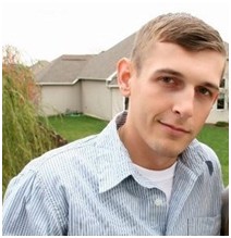 Joshua wearing striped button up shirt outside with house in background