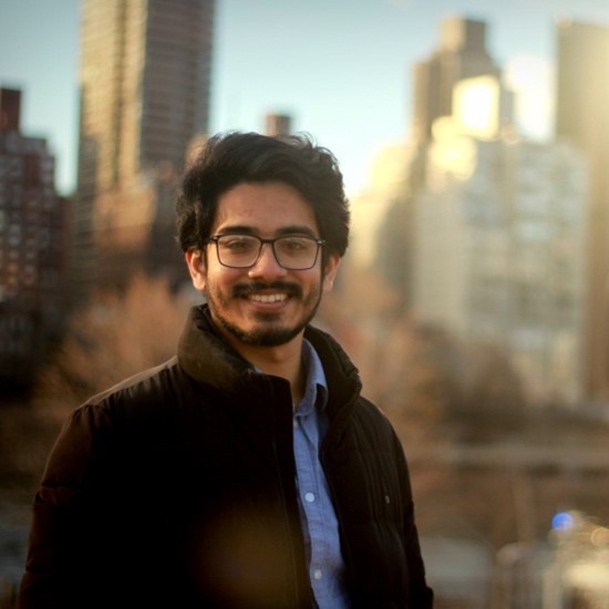 A smiling color photo of Sk. Abu Talha wearing a black jacket and a blue shirt in front of a city skyline.