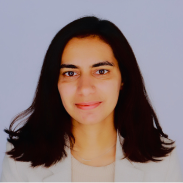 A smiling photo of Manisha Sheokand with dark hair, wearing a white blazer in front of a neutral background.