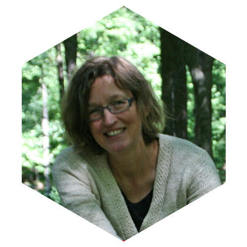 Hexagon shaped Photo of Lora Arduser outside in the woods with green leaves and trees behind her, Image links to Faculty and social media page